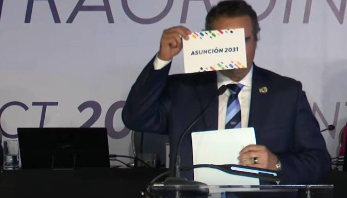 Michael Chambers, presidente da Comissão Jurídica da Associação dos Comitês Olímpicos Nacionais, exibe papel que confirma de vitória de Assunção para o Pan-2031
             -       
        Reprodução/Cazé TV