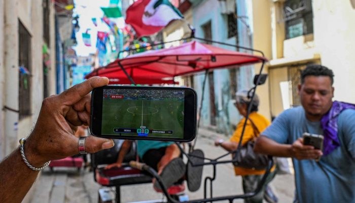 Torcedores cubanos da seleção mexicana de futebol assistem à partida de abertura da Copa do Mundo entre México e África do Sul em seus celulares, em Havana
             -       
        Yamil Lage /AFP